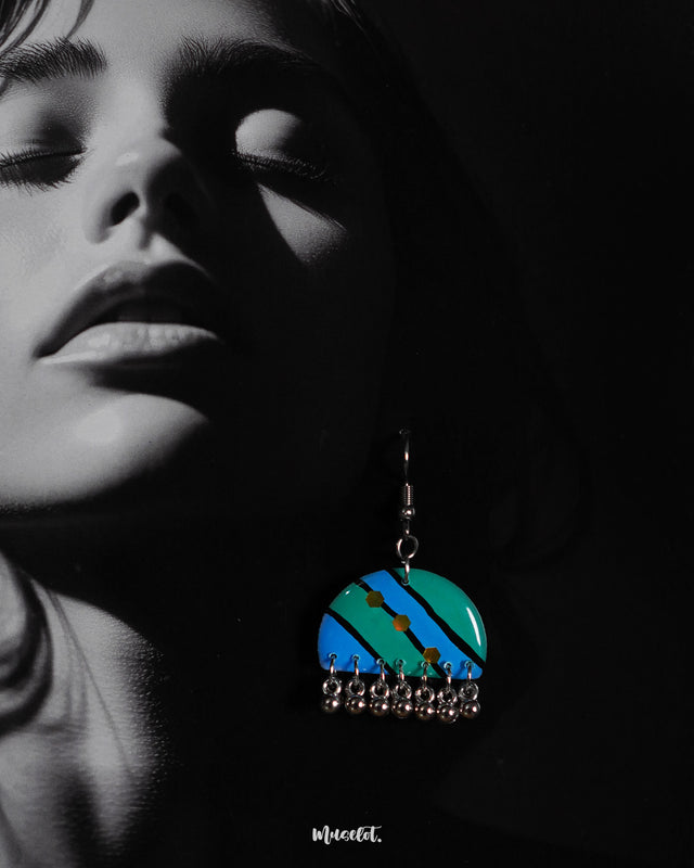 Close-up of a woman wearing the Jaltarang drop earrings, highlighting the bold blue and green diagonal stripes, yellow dot detailing, and delicate silver ghungroo accents that create a rhythmic, eye-catching appeal—Muselot
