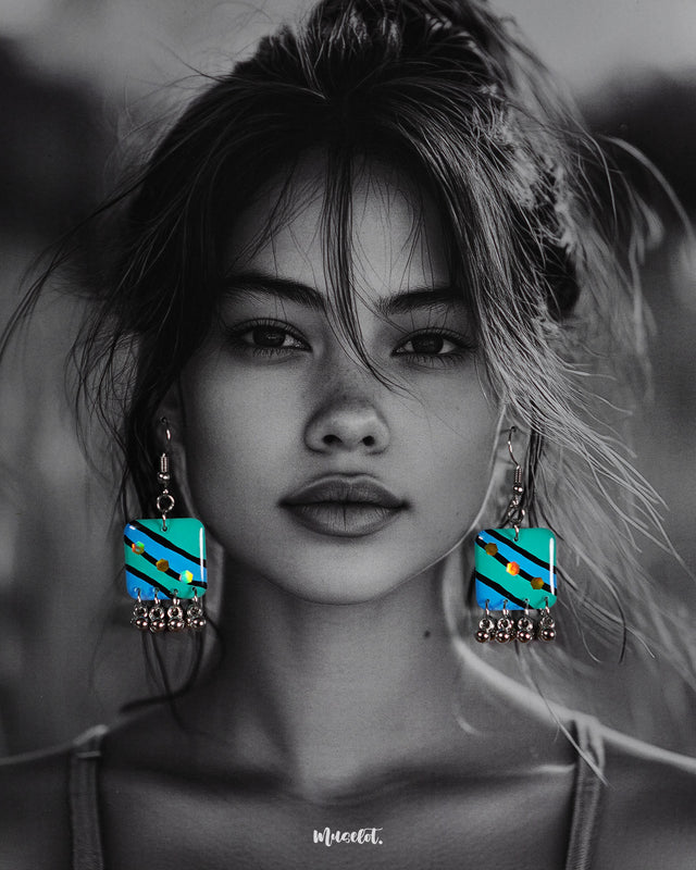A woman models the Jaltarang strip drop earrings, featuring vertical blue and green hand-painted enamel strips with delicate silver ghungroos swaying at the ends, creating a playful yet elegant statement—Muselot.