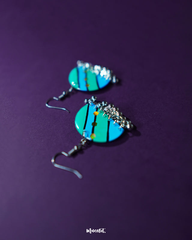 A pair of Jaltarang strip earrings displayed against a soft purple background, featuring sleek vertical lines and subtle metallic sheen that adds a modern yet cultural charm—Muselot.