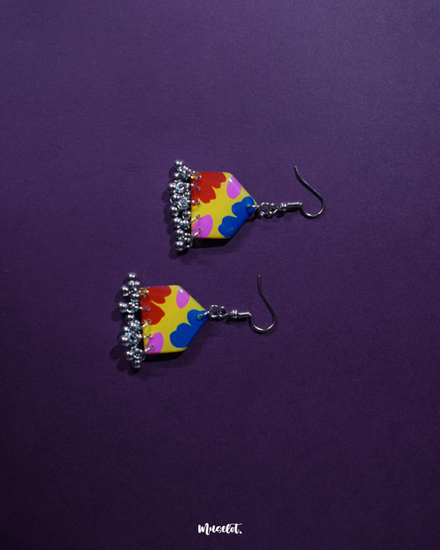 Jharokhe multicolor floral hook earrings placed against a deep purple background, featuring a bold mix of red, yellow, blue, and pink floral patterns with silver ghungroo dangles that highlight their handcrafted vibrance — Muselot.