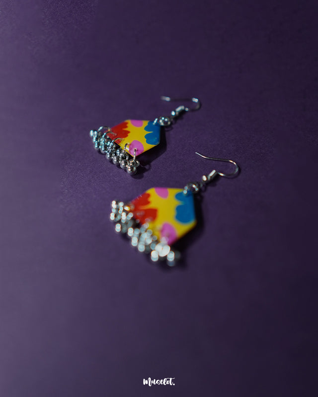 A pair of Jharokhe multicolor floral hook earrings resting on a purple surface, highlighting the bold color palette, delicate floral design, and dangling ghungroo elements that bring playful elegance — Muselot.