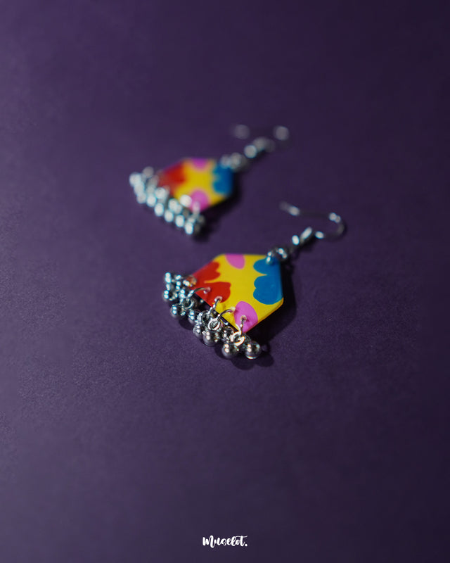 Jharokhe multicolor floral hook earrings displayed upright on a soft purple background, showcasing their handcrafted detailing, vibrant floral motifs, and metallic finish that adds a festive and artistic flair — Muselot.