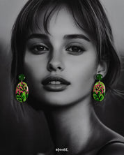 A woman wears the Kalibaan handmade drop earrings, highlighting the playful contrast of lush green and bright pink floral art. The hand-painted design stands out beautifully, showcasing the charm of nature-inspired craftsmanship in a bold and wearable style — Muselot