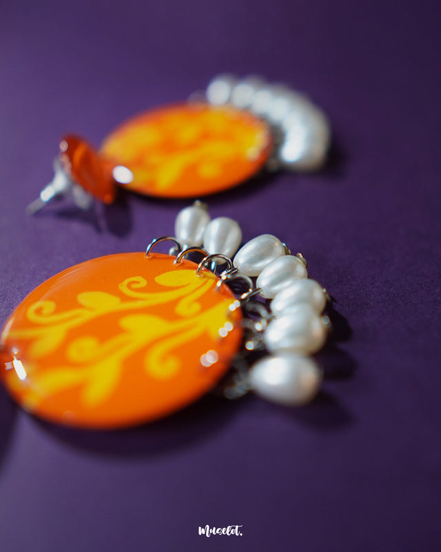 A vibrant close-up of the Kesarbaan earrings showcasing their hand-painted orange and yellow design with delicate white pearl drops that lend a festive and elegant touch – Muselot.