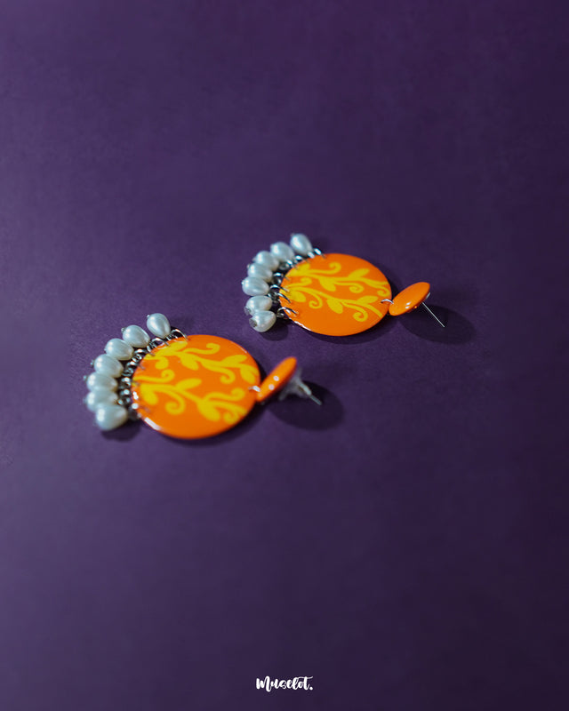 Kesarbaan earrings displayed in a flatlay, highlighting their symmetrical orange and yellow motifs with pearl drop detailing – perfect for adding a handcrafted charm to ethnic or boho looks – Muselot.