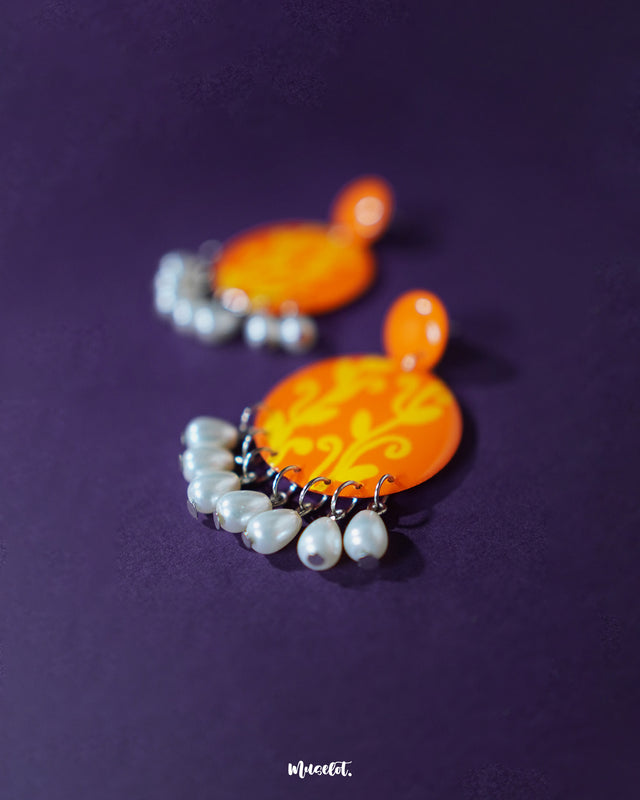 The Kesarbaan orange and yellow drop earrings feature a bright floral motif with a playful splash of color, finished with classic pearls that sway gently, offering a handcrafted blend of tradition and trend — Muselot.