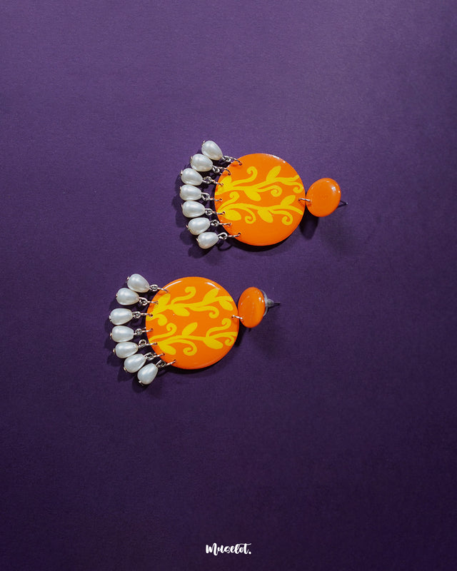 These Kesarbaan orange and yellow drop earrings highlight their unique layered design — vibrant floral accents paired with glistening pearls create a festive, eye-catching look that’s perfect for uplifting any outfit — Muselot.