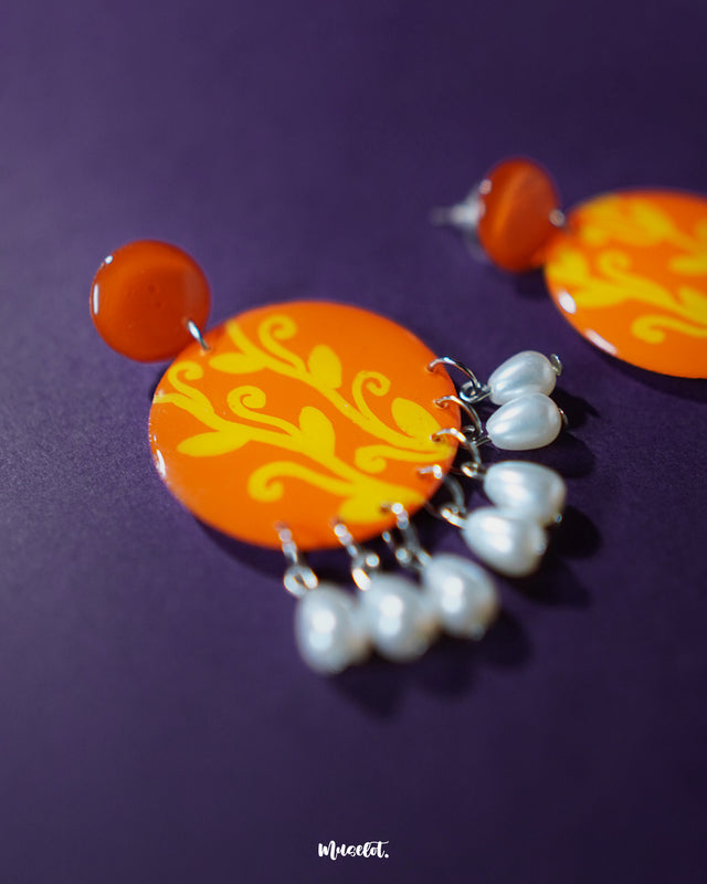 The Kesarbaan orange and yellow drop earrings showcase an elegant downward cascade of floral elements with pearl detailing, blending warm tones and intricate craftsmanship for a graceful and festive aesthetic — Muselot.