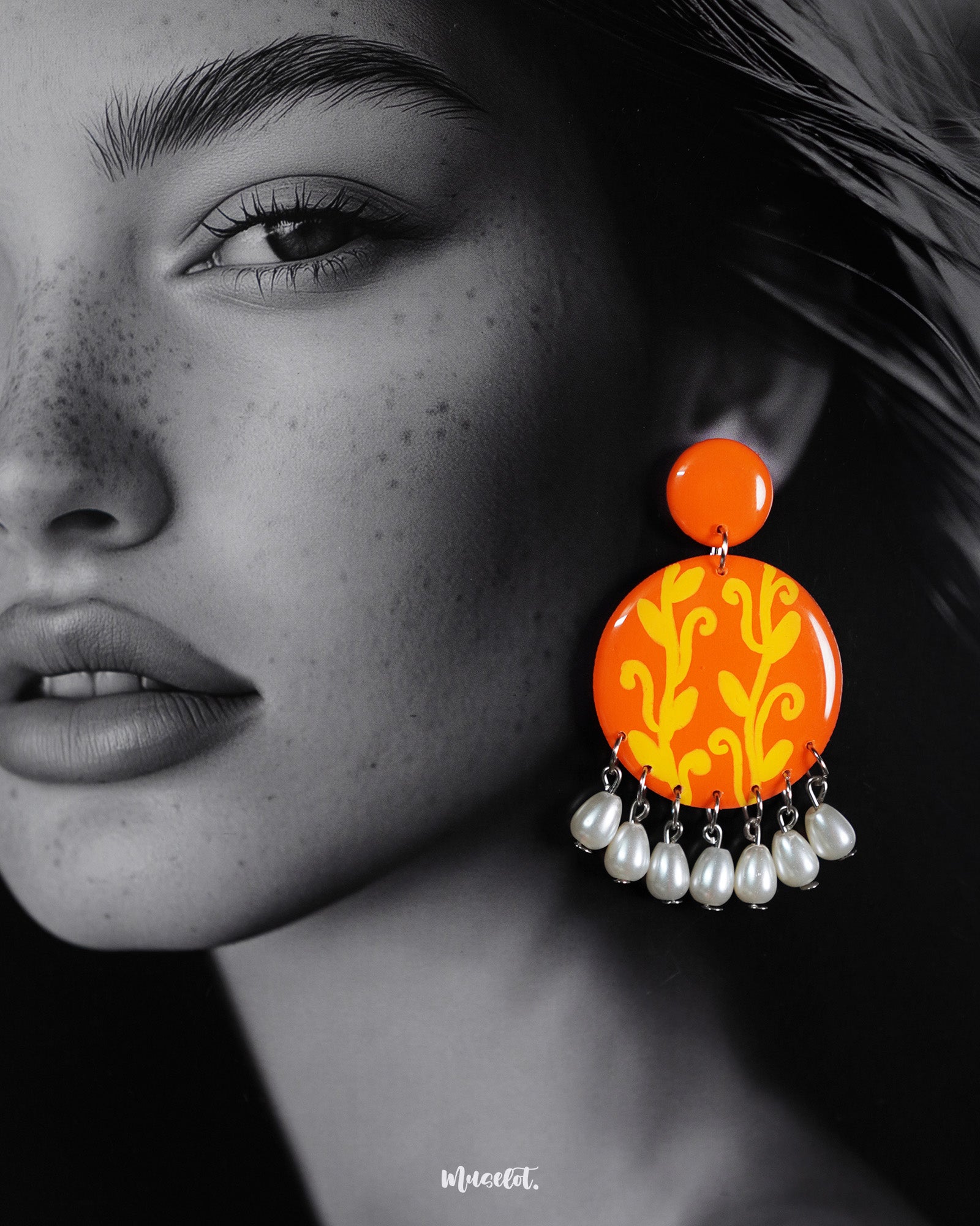 A woman wearing the Kesarbaan pearl drop earrings, where the vibrant orange discs with yellow folk motifs draw the eye, while the dangling white pearls softly frame her jawline, adding a graceful charm to her look – Muselot.