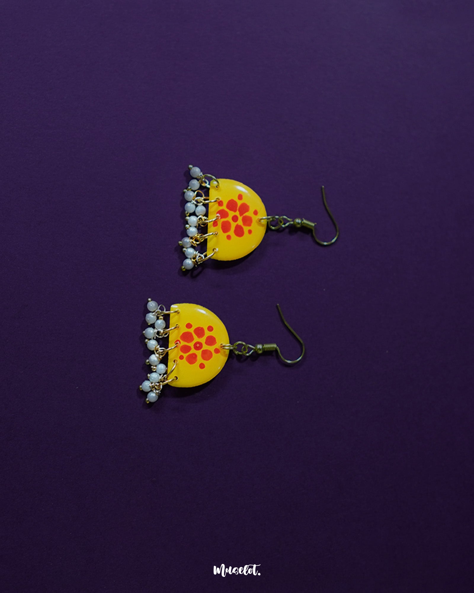 Kesarika floral yellow hook earrings, set against a rich purple background, with vibrant red petals and fine detailing that beautifully contrast with the backdrop, radiating warmth and graceful elegance — Muselot.