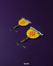 Kesarika floral yellow hook earrings, resting against a deep purple backdrop, featuring bright red floral elements and fine handcrafted details that exude a joyful, vibrant charm — Muselot.