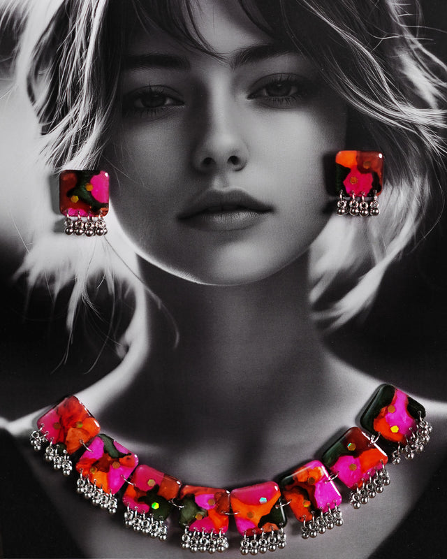 Model wearing the Khushk Gul handmade floral necklace set, featuring a silver chain necklace and matching square stud earrings with vivid pink, orange, and green abstract floral patterns and silver bead accents, stylishly displayed to emphasize its bold, artisanal charm – Muselot.