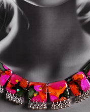 Close-up of model wearing the Khushk Gul handmade floral necklace, showcasing vibrant pink, orange, and green abstract floral-patterned square charms with delicate silver bead accents on a silver chain, highlighting the intricate craftsmanship and vivid colors – Muselot.