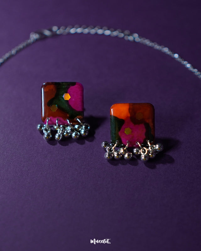 Close-up of the Khushk Gul handmade floral earrings, featuring square charms with vibrant pink, orange, and green abstract floral patterns accented by delicate silver beads, highlighting the intricate detailing and rich colors – Muselot.