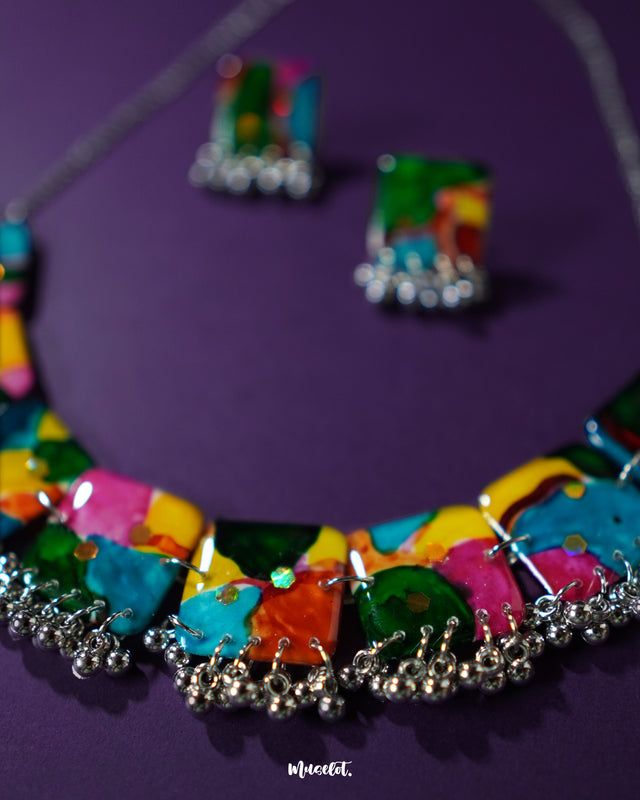 Zoomed-in view of the colorful jewelry set from Muselot, laid against a rich purple background. The vibrant mix of multicolored beads and playful design elements are in sharp focus, highlighting the lively boho spirit and handcrafted artistry — Muselot.