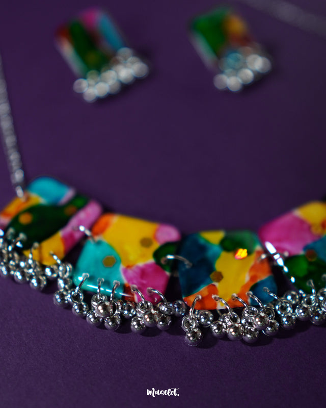 A vibrant boho-style jewelry set featuring multicolored beads and playful motifs, laid out neatly on a deep purple background. The vivid hues and eclectic arrangement highlight its artisanal charm and free-spirited aesthetic — Muselot.