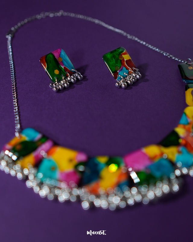 A flat lay of the colorful jewelry set, displayed on a rich purple background. The set includes a necklace and earrings adorned with a mix of vibrant beads and earthy elements, showcasing its handcrafted boho aesthetic and joyful color palette — Muselot