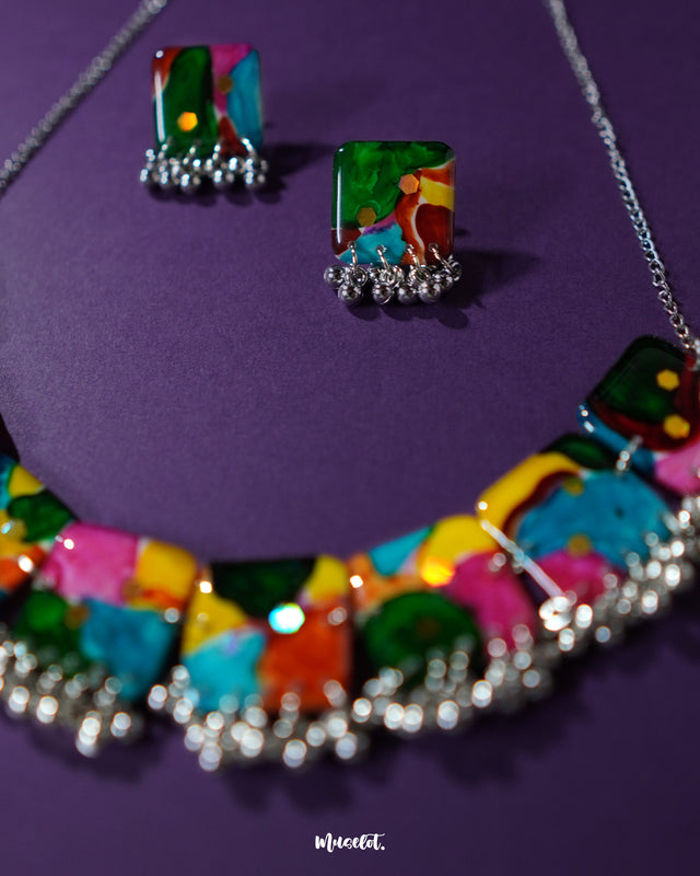 The Kohsar colorful jewelry set laid out on a rich purple backdrop, showcasing its bohemian style with vibrant beads in assorted hues, ornate metal elements, and coordinated earrings — a statement ensemble full of artistic flair — Muselot.