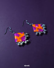 The Laalsavera hook earrings, featuring a sleek design and placed against a deep purple background, offer a sophisticated look — Muselot.