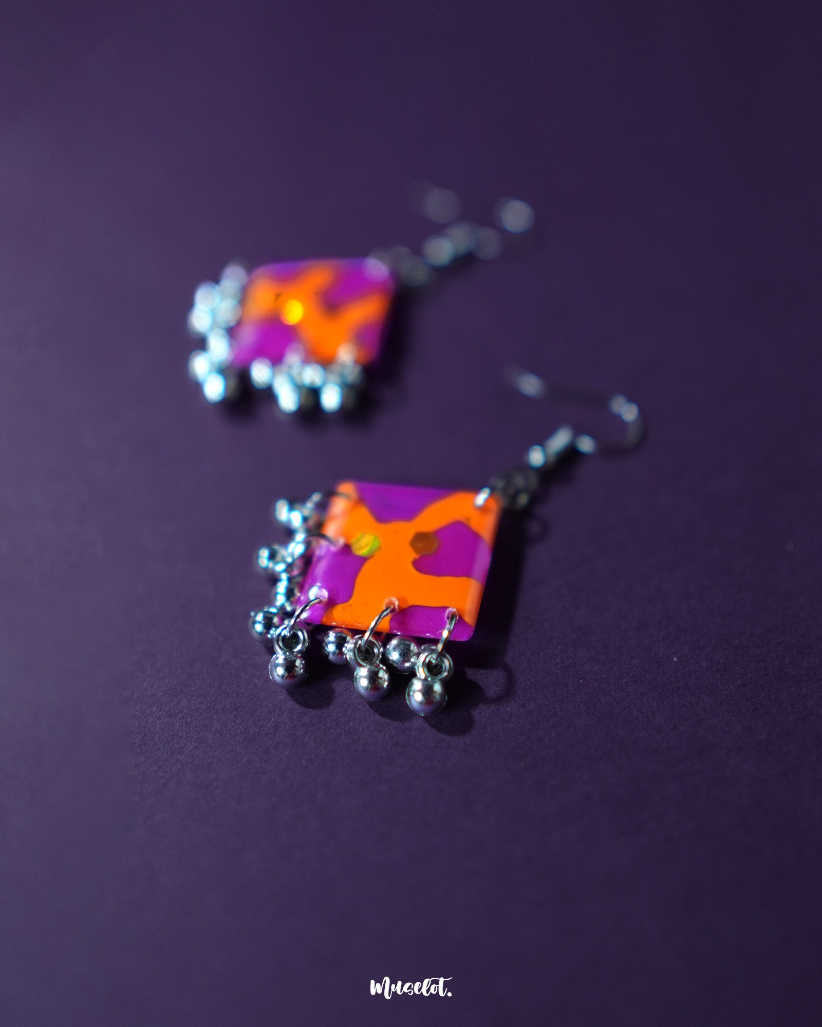 The Laalsavera hook earrings flaunt a unique artistic flair, with their bold, abstract shape highlighted perfectly against a moody purple background -Muselot.