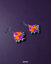 The Laalsavera hook earrings, elegantly displayed with a purple background, highlight their sleek design — Muselot.