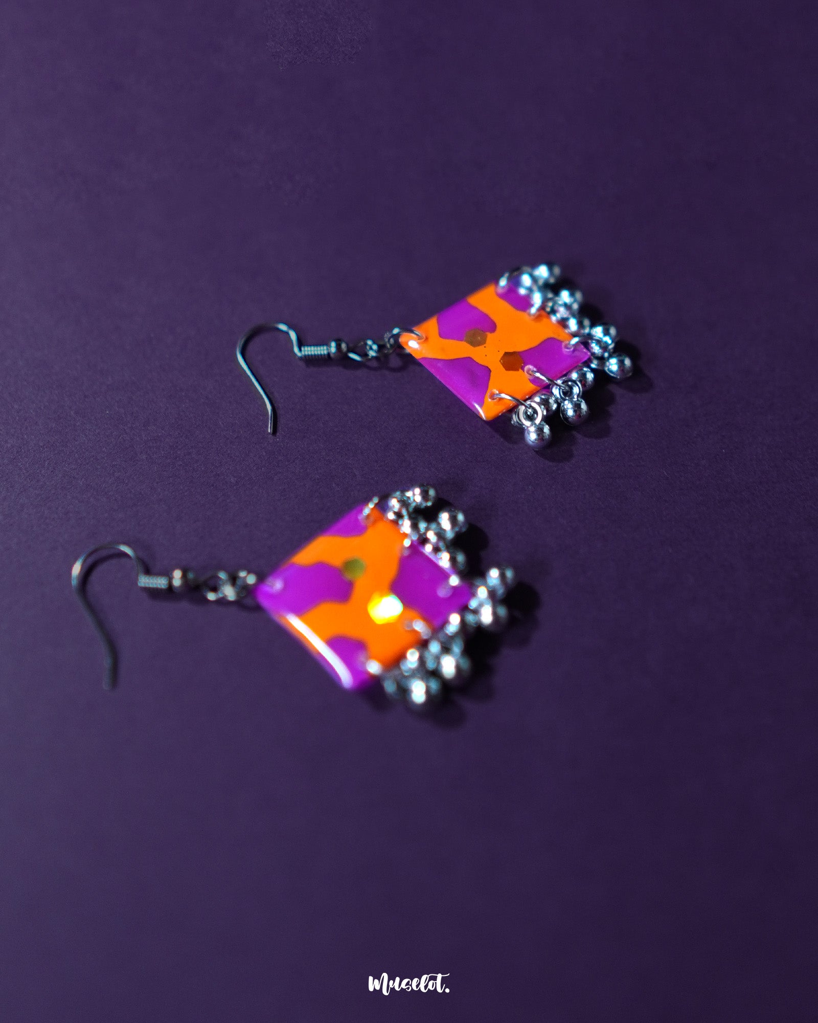The Laalsavera hook earrings, set against a rich purple background, showcase a refined and modern style-Muselot.