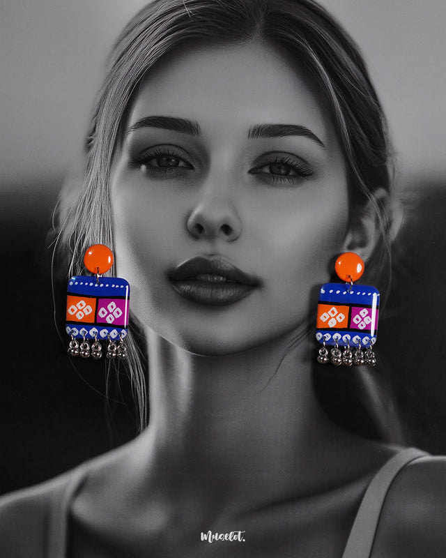 Model wearing the Leheriya boho earrings, featuring bright orange round studs attached to vibrant blue rectangular drops with orange and magenta blocks, decorated with white geometric patterns and dotted detailing, finished with dangling silver beads, highlighting their colorful and eclectic charm – Muselot.