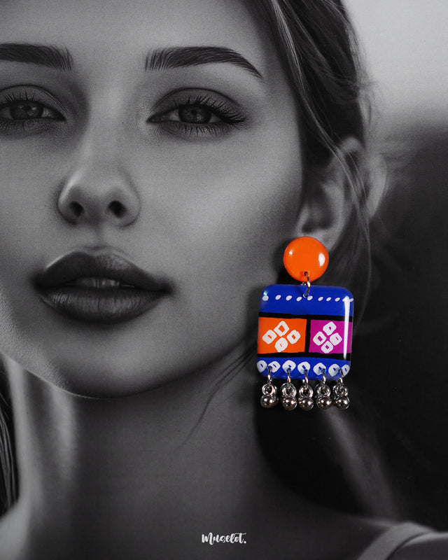 Close-up of model wearing the Leheriya boho earrings, showcasing bright orange round studs connected to blue rectangular drops with orange and magenta blocks, detailed with white geometric patterns and dotted accents, finished with dangling silver beads, capturing their vibrant and artistic design – Muselot.