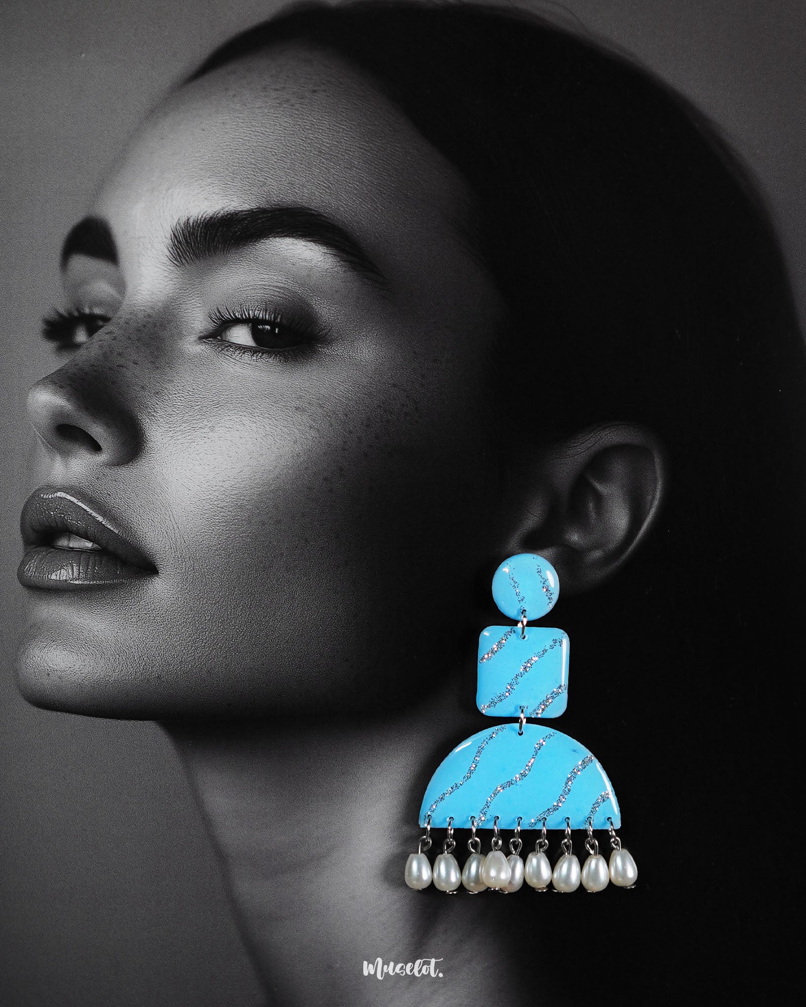A model wearing the Lehrbaan drop earrings showcases their vibrant sky blue color and unique geometric design. The dangling white pearls add graceful movement, while the glittery silver waves catch the light, making them a standout accessory for festive or artistic looks — Muselot.