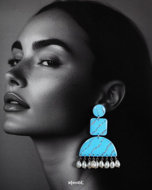 A model wearing the Lehrbaan drop earrings showcases their vibrant sky blue color and unique geometric design. The dangling white pearls add graceful movement, while the glittery silver waves catch the light, making them a standout accessory for festive or artistic looks — Muselot.
