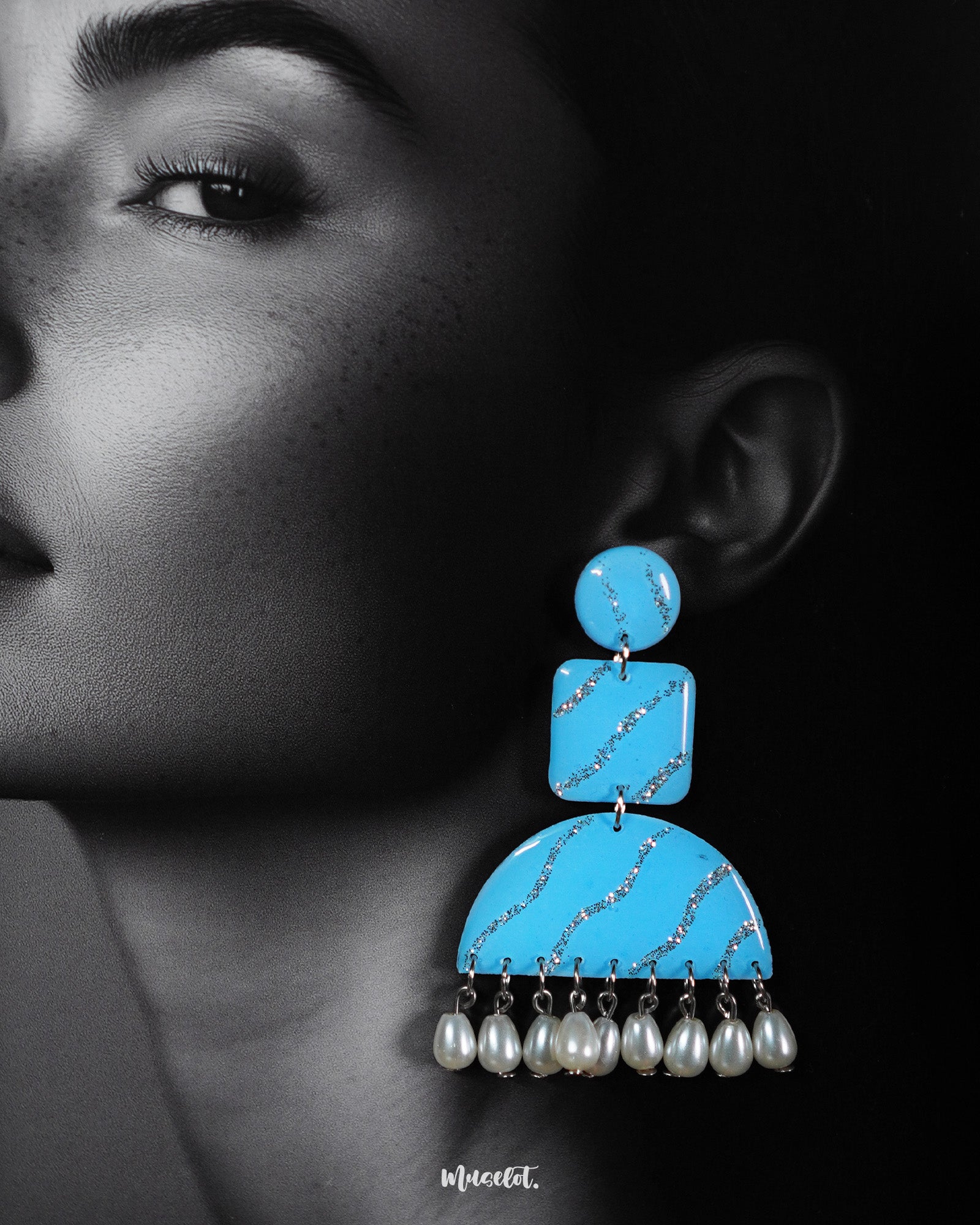 A close-up of the model wearing the Lehrbaan drop earrings highlights the intricate details of the design — from the glittery silver streaks on the sky blue base to the soft sheen of the hanging pearls. The earrings exude a playful elegance, perfect for making a chic statement — Muselot.