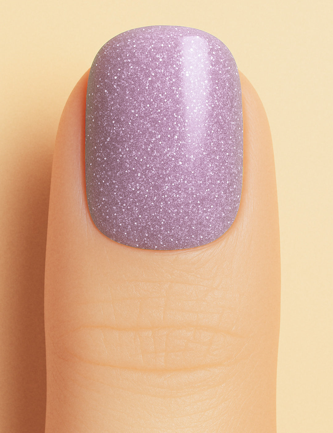 A close-up shot of a model’s finger wearing Lilac Dust Glitter nail stickies, showcasing a soft pastel lilac shade infused with fine glitter specks, creating a subtle yet elegant sparkle with a smooth, glossy finish – Muselot.