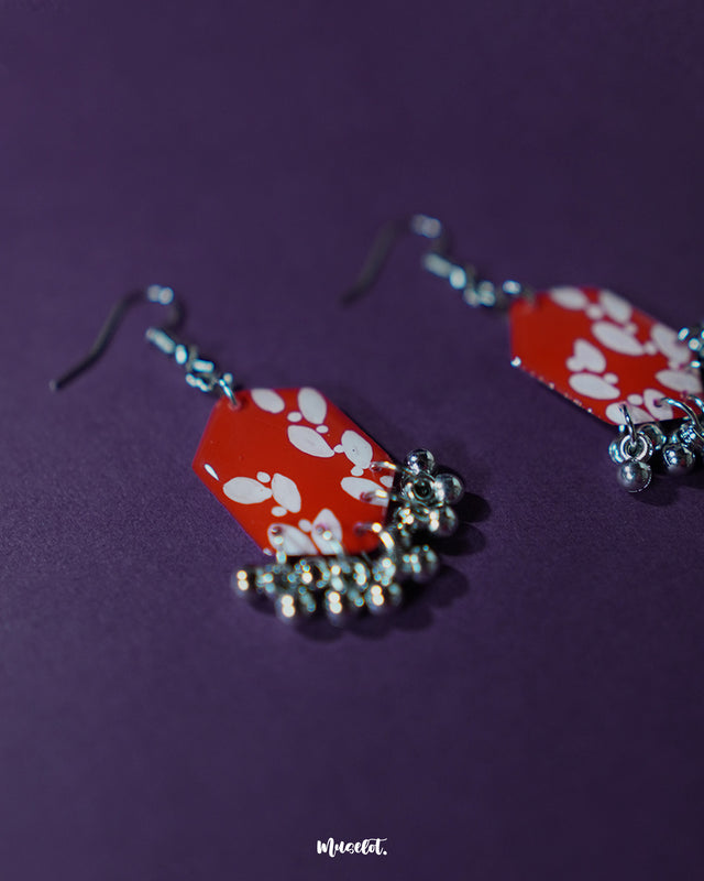 A close-up view of the Mehar red floral hook earrings from Muselot — highlighting the fine brushwork of the white floral motifs on vivid red enamel drops, with metallic ghungroos accentuating the handcrafted detail and traditional artistry.