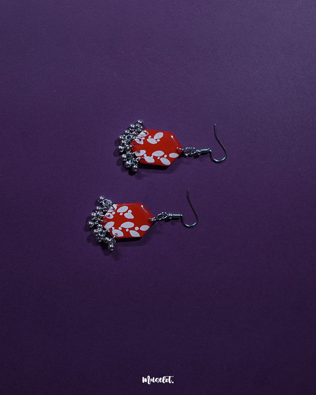 The Mehar red floral hook earrings presented in a minimal setup, highlighting the bold hexagonal shape, striking red hue, and delicate white floral detailing, with metallic ghungroos adding a subtle traditional charm to the contemporary design.