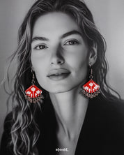 A model styles the Meherbaan red floral earrings with poise, showcasing the vibrant red hand-painted tulip design and silver ghungroo detailing that lend a charming ethnic flair — Muselot.