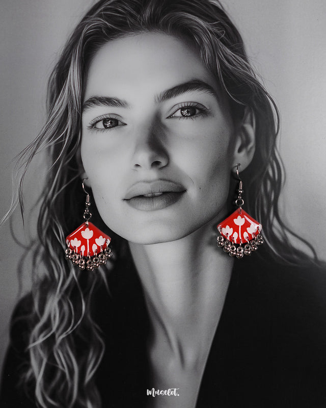 A model styles the Meherbaan red floral earrings with poise, showcasing the vibrant red hand-painted tulip design and silver ghungroo detailing that lend a charming ethnic flair — Muselot.