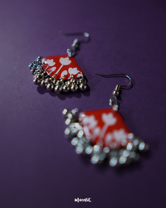 Close-up of the Meherbaan red floral hook earrings featuring hand-molded red tulip petals with intricate silver ghungroo detailing, highlighting traditional craftsmanship and showcasing festive flair — Muselot.