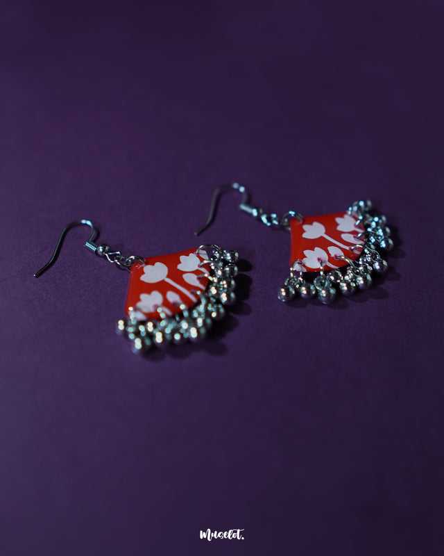 Meherbaan red floral hook earrings displayed flat with hand-sculpted tulip petals and dangling silver beads, highlighting their artisanal texture and showcasing vibrant traditional elegance — Muselot.