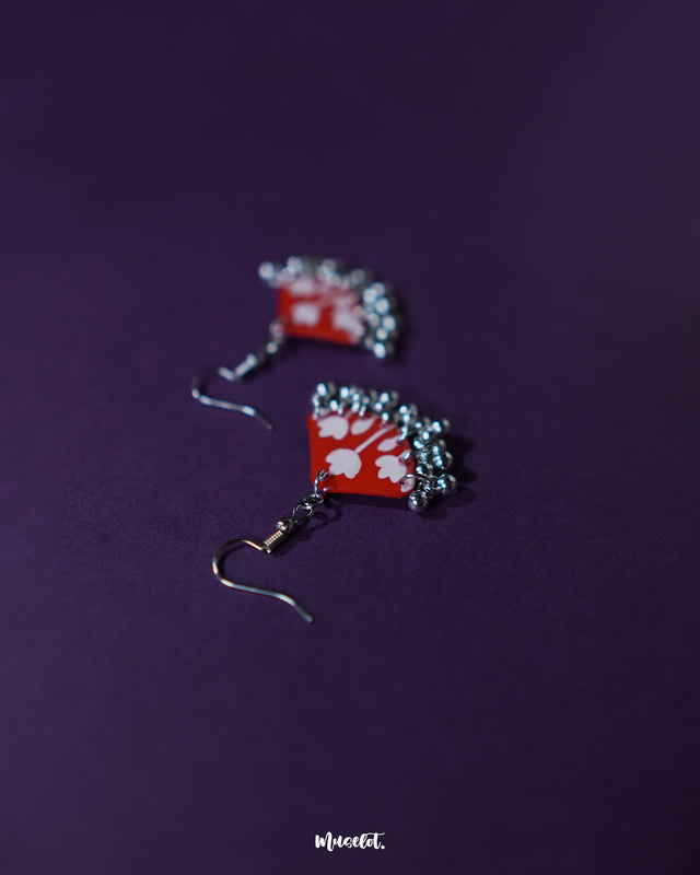 A pair of Meherbaan red floral hook earrings laid flat against a neutral backdrop, capturing the vivid red hues and delicate floral detailing that make these earrings a vibrant style statement — Muselot.