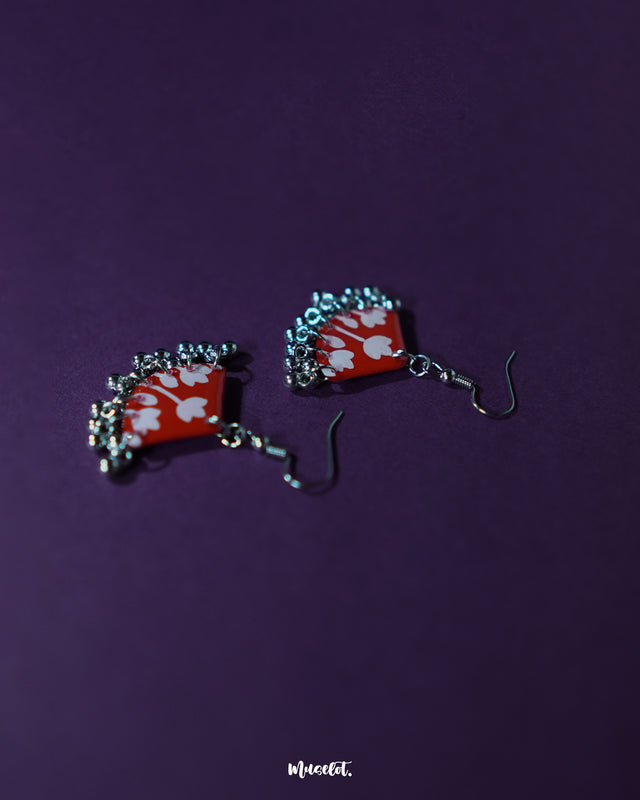 Meherbaan red floral hook earrings placed flat against a soft-toned background, showcasing their blooming red floral design with detailing and graceful hook finish — Muselot.
