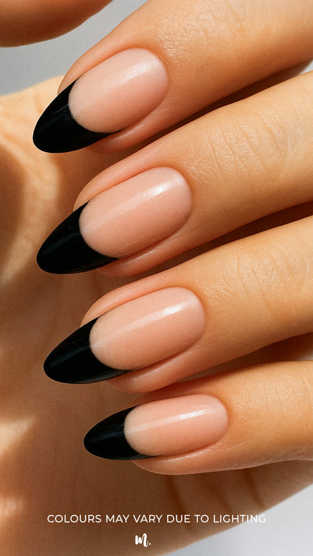 A close-up of a model’s hand wearing Midnight Tiara French Tip nail stickies, featuring a sleek black French tip design over a natural nude base. The glossy finish highlights the sharp contrast, giving a bold yet elegant twist to the classic French manicure style – Muselot.
