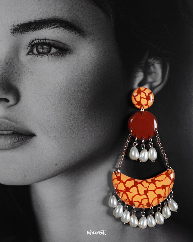 Close-up of a model wearing the Mittika chandbali earrings, highlighting the vibrant crackle-patterned orange arcs and elegant pearl drops that dangle gracefully — a handcrafted fusion of earthy tones and playful movement — Muselot.