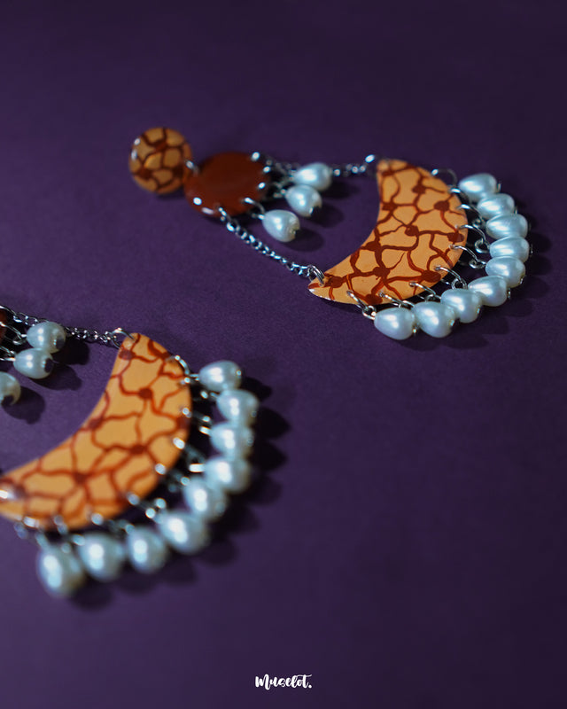 The Mittika chandbali earrings lie gracefully on a neutral backdrop, highlighting their crescent-shaped frame adorned with intricate motifs and white pearl accents that exude ethnic charm and festive elegance — Muselot.