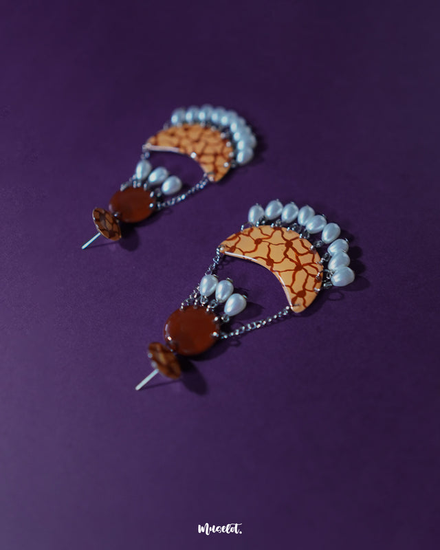 Mittika chandbali earrings displayed against a deep purple background, showcasing their bold orange crackle pattern and delicate pearl danglers for a vibrant, handcrafted charm — Muselot.