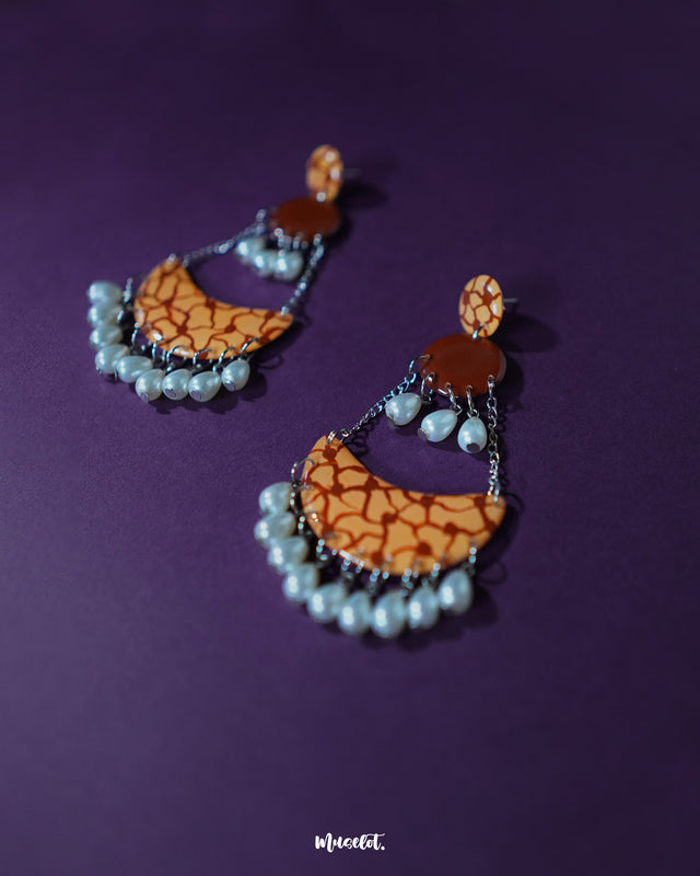 The Mittika chandbali earrings rest on a textured brown surface, highlighting the intricate floral enamel work, clustered pearls, and oxidized silver detailing that together create a vintage yet vibrant appeal — Muselot.