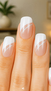 A model’s hand showcasing the Moonlit Wave White French Nail Art from Muselot. The nails feature a modern diagonal French tip in crisp white, highlighted with a fine silver glitter accent line, contrasted against a glossy nude base. The elegant design gives a polished, sophisticated finish perfect for everyday chic or special occasions.