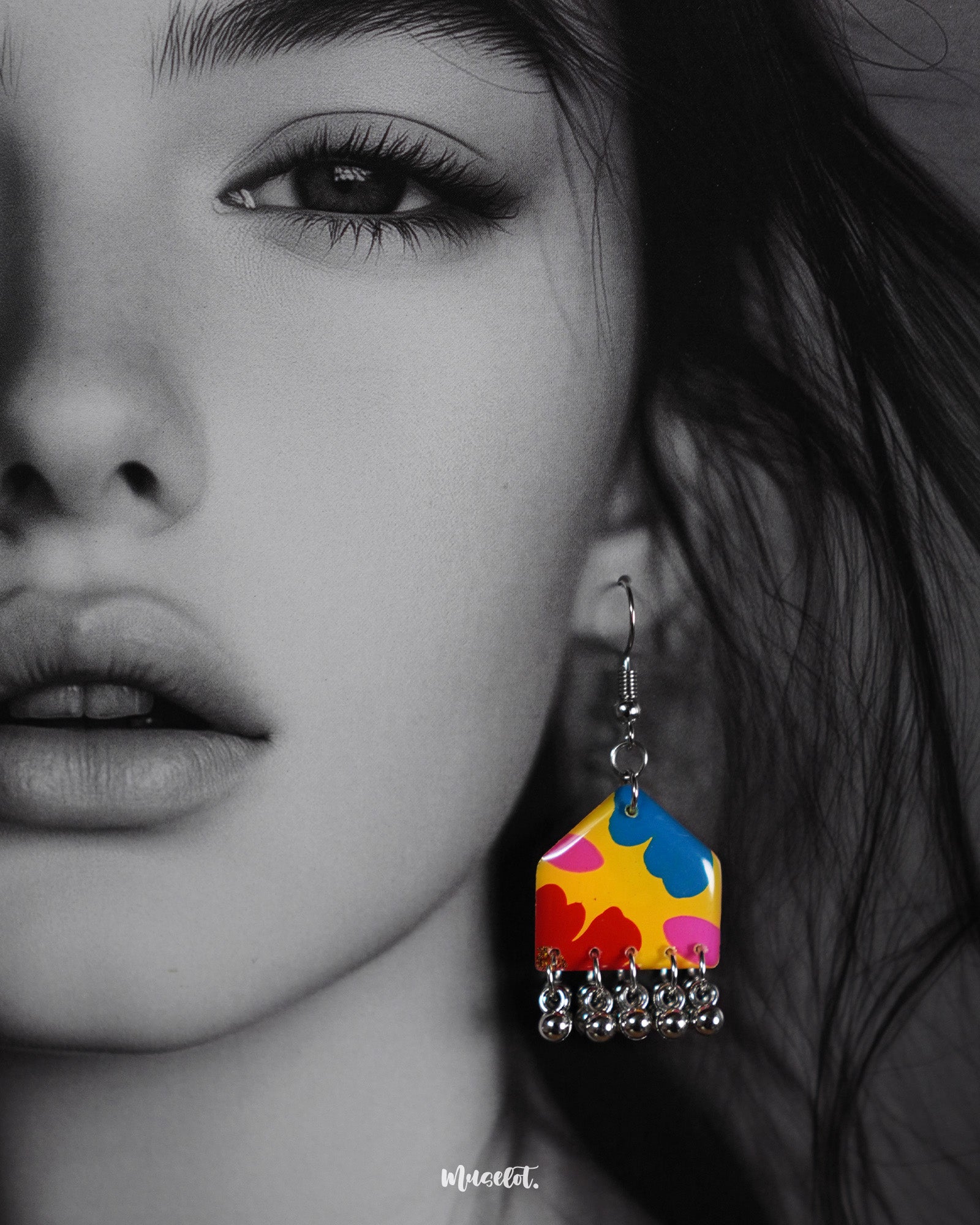 A close-up of a model wearing the Jharokhe multicolor floral earrings, highlighting the vivid floral patterns in yellow, red, blue, and pink, with delicate silver ghungroos swaying at the bottom, capturing a cheerful and artistic vibe — Muselot