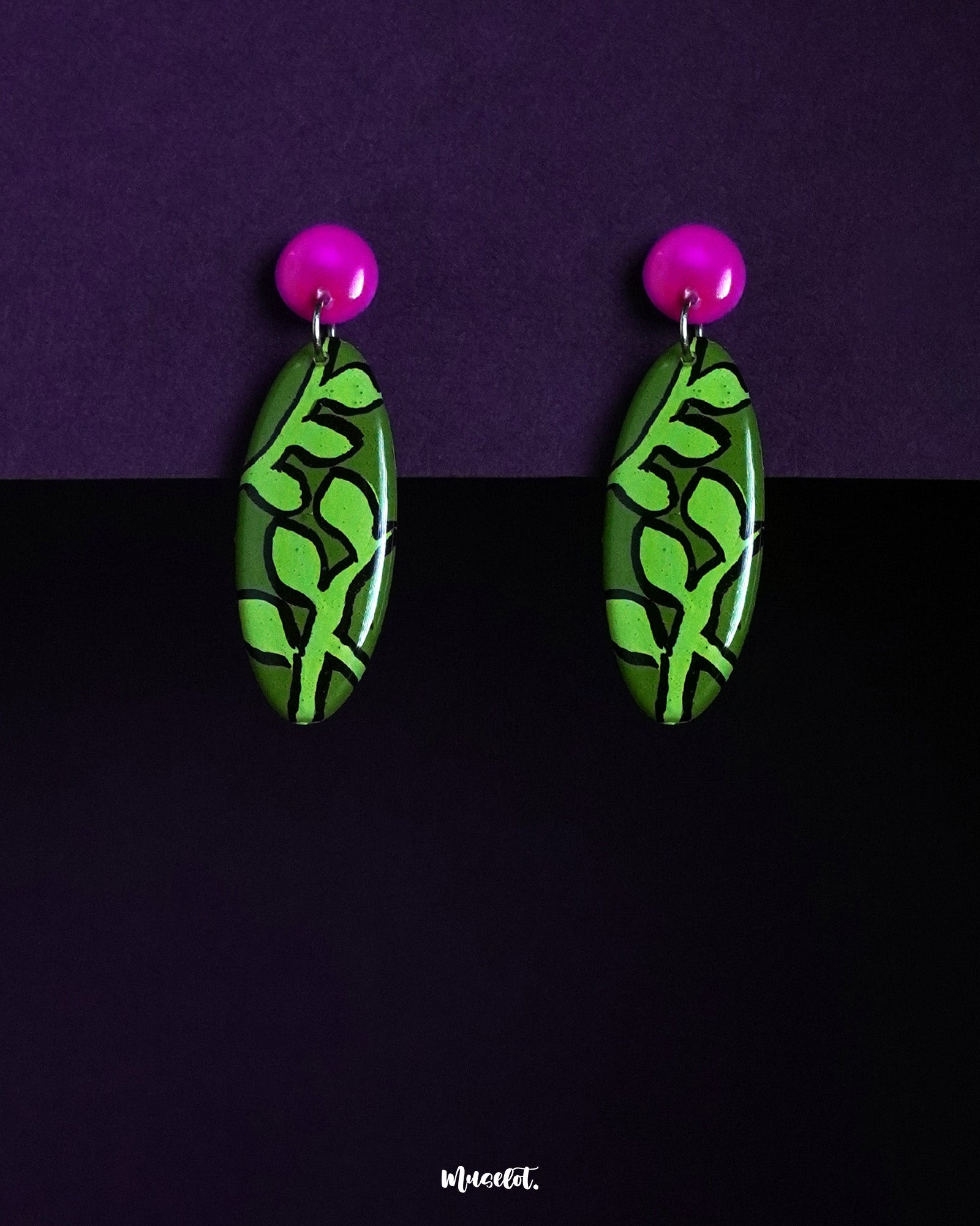 A pair of Naghma leaf drop earrings featuring a vivid green leaf motif on elongated oval shapes, topped with glossy magenta studs, highlighting the bold contrast and showcasing their artistic, nature-inspired design — Muselot.