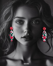 A woman wearing the Nargis handmade floral drop earrings with her hair tucked back, highlighting the vivid pink floral pattern and the glossy finish that showcases the hand-painted craftsmanship and playful elegance — Muselot.