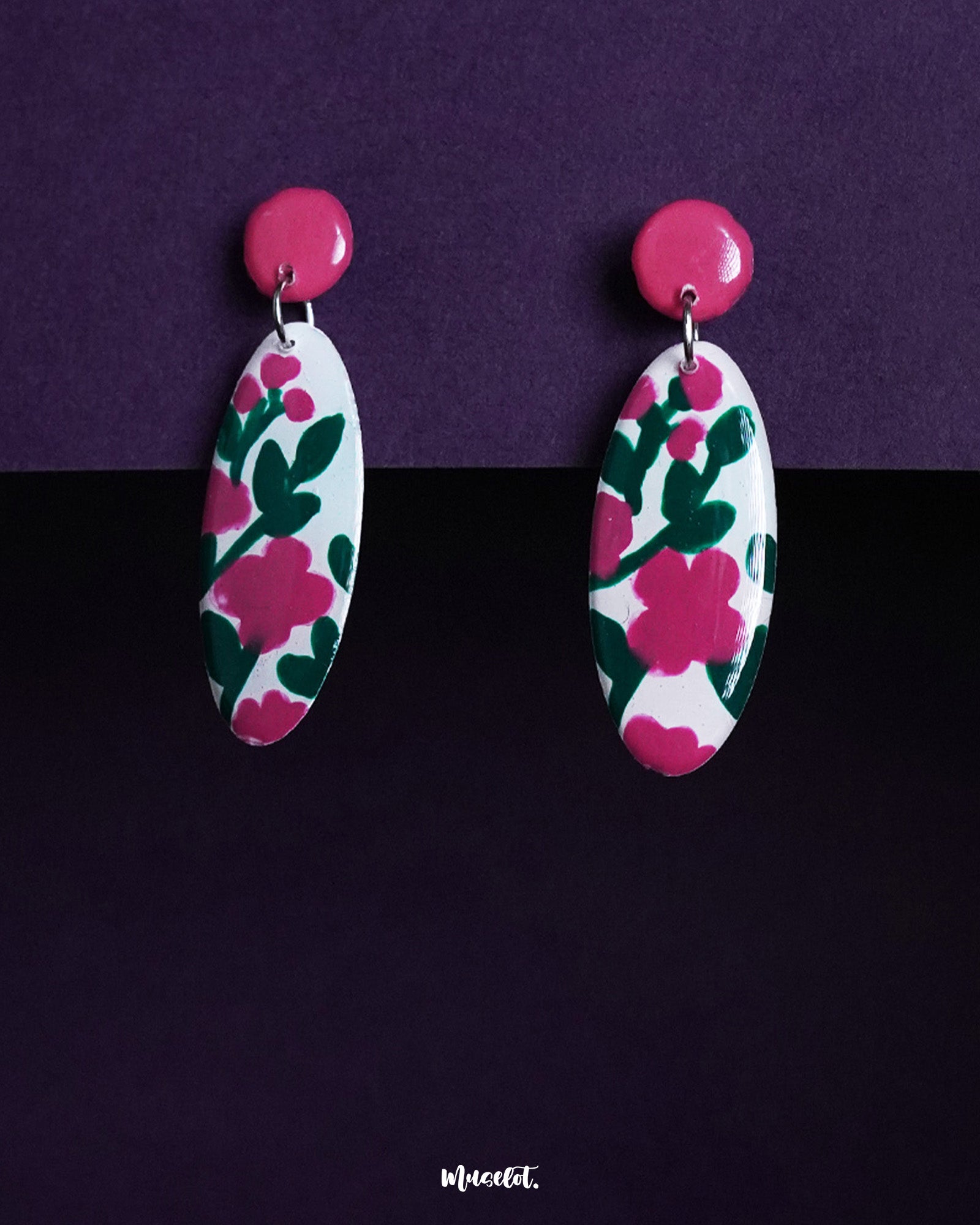 Nargis floral drop earrings displayed against a dual-tone purple background, highlighting the hand-painted pink and green floral patterns on white ovals, showcasing the charm of handmade artistry — Muselot.